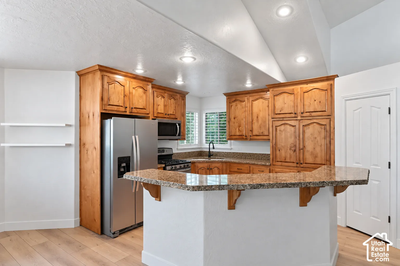 Kitchen featuring wood cabinetry, stainless steel appliances, a corner sink, and a breakfast bar with stone countertops