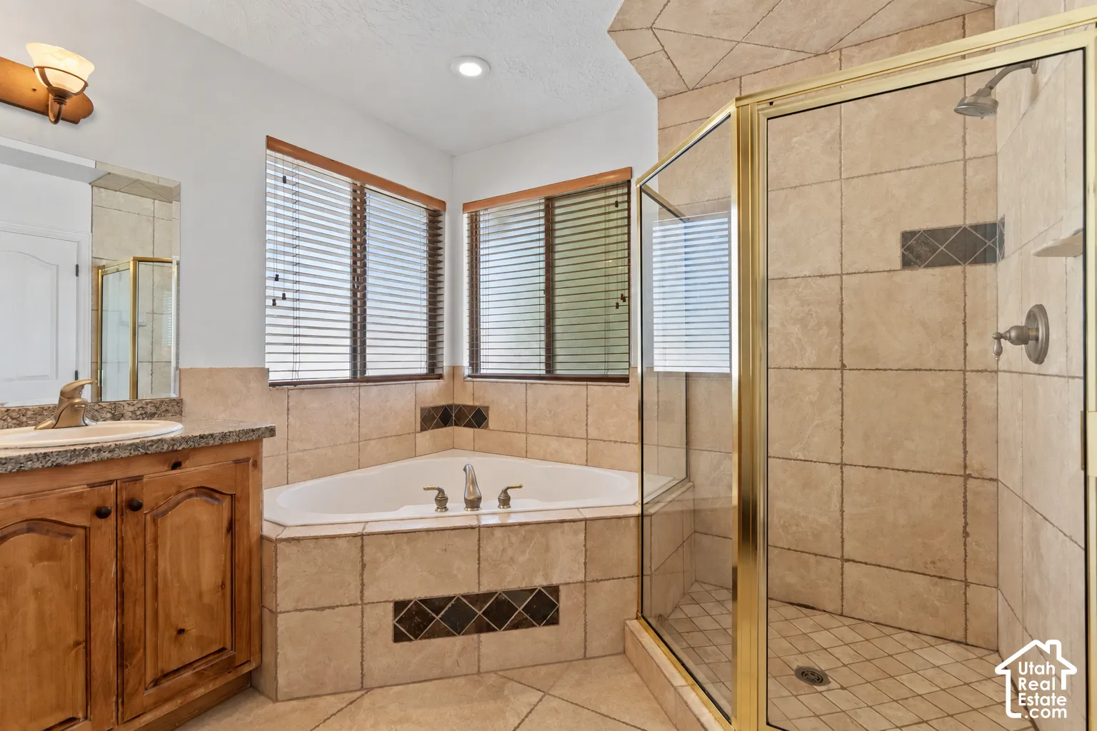 Tiled bathroom featuring a corner soaking tub and an enclosed shower with a glass and brass frame