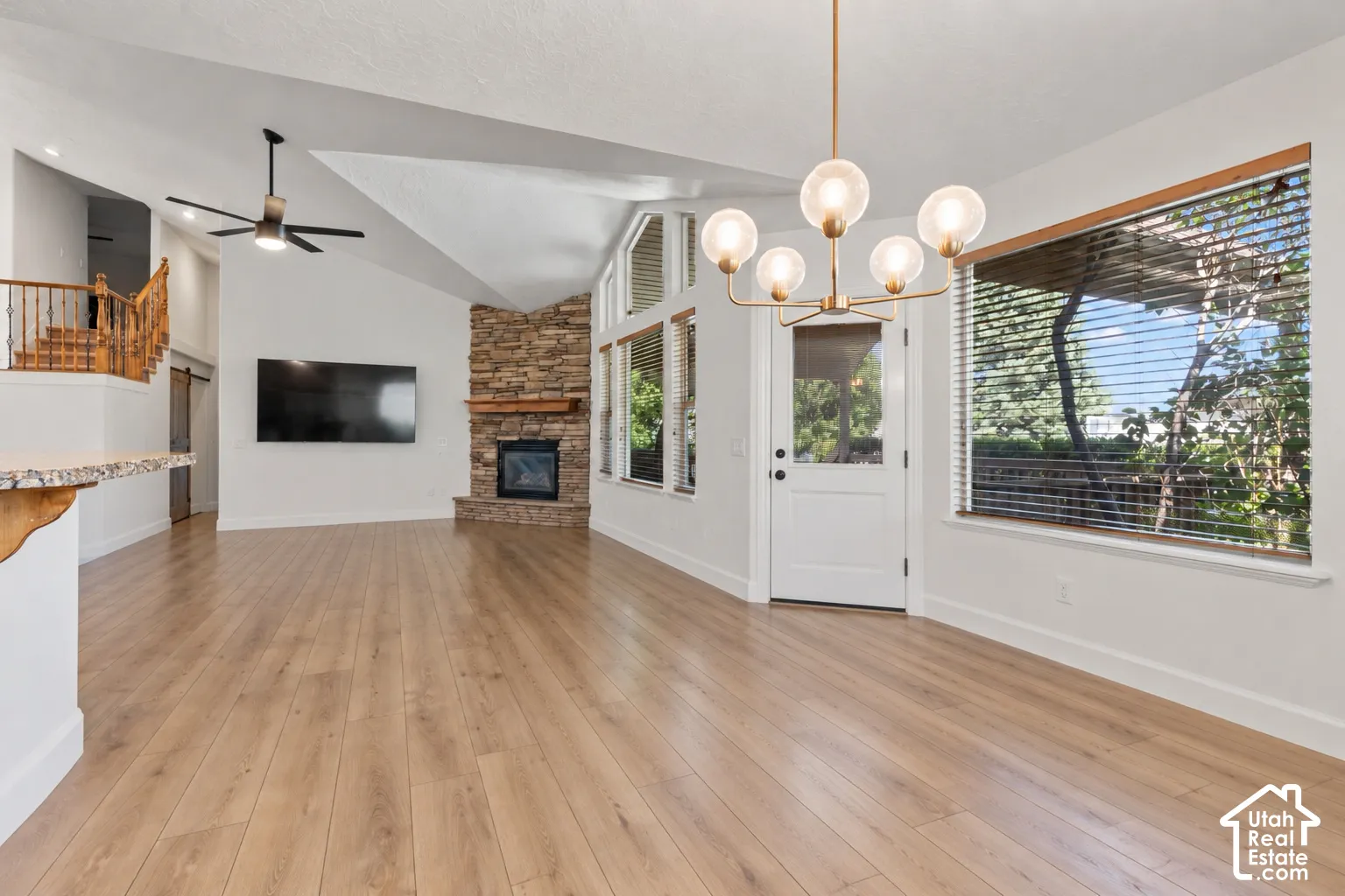Vaulted ceilings, wood-finish flooring, stone-clad fireplace with mantel, and a modern chandelier