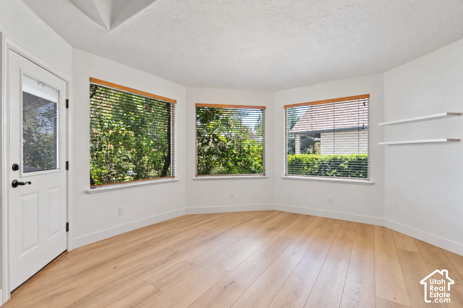 Bay window with natural wood trim, light wood-finish flooring, white walls, and built-in white shelving