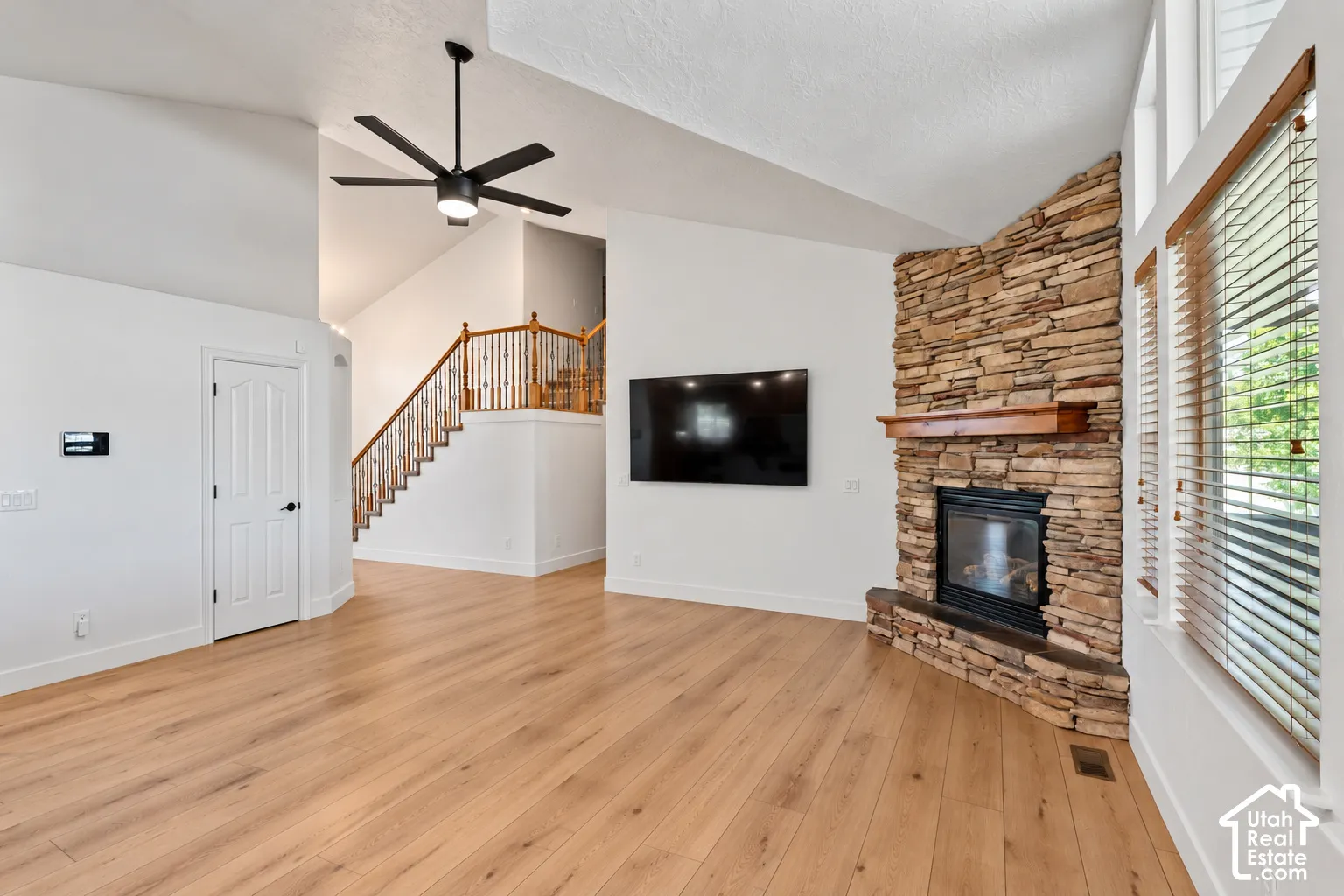 Vaulted ceilings, wood-finish flooring, stone-clad fireplace with a wood mantle, and a staircase with wood handrails and balusters