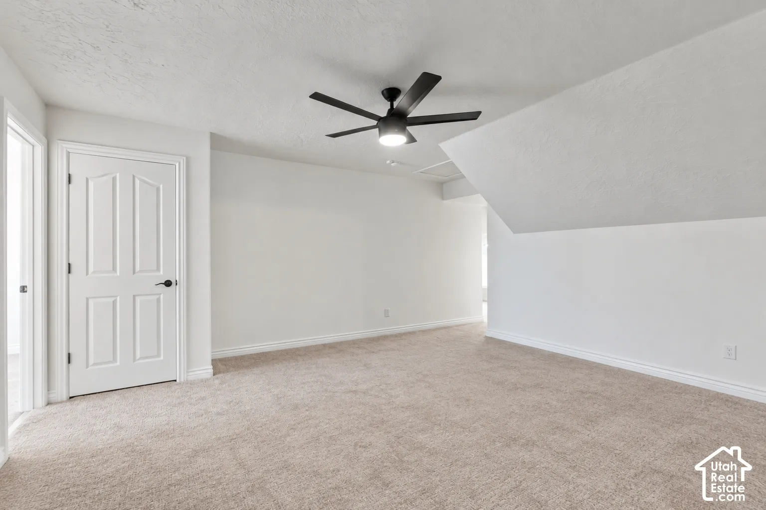 Carpeted flooring, vaulted ceiling, white interior paint, contemporary ceiling fan, and panel door with dark hardware