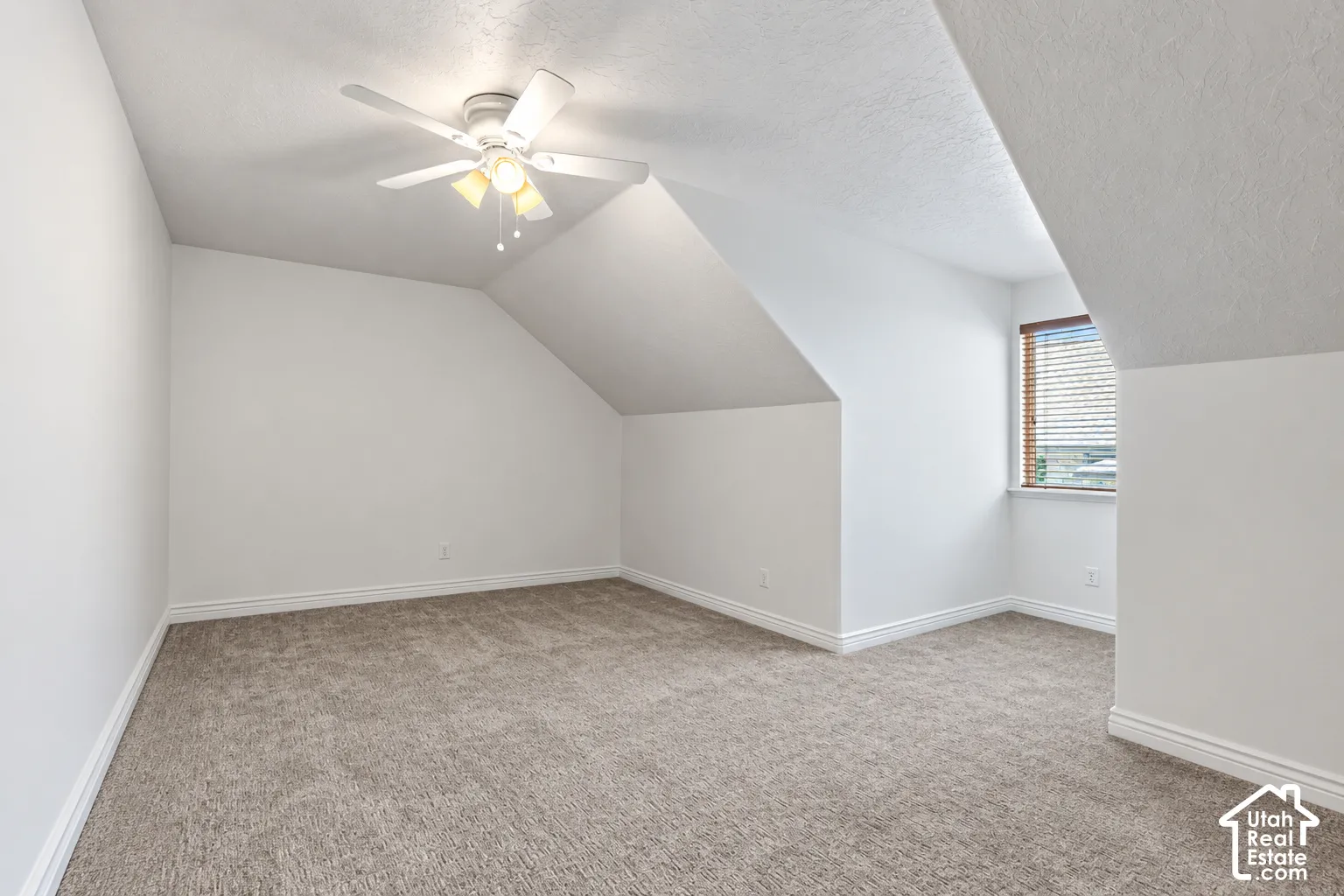 Carpeted room featuring a ceiling fan with integrated lighting, a window with blinds, and white trim