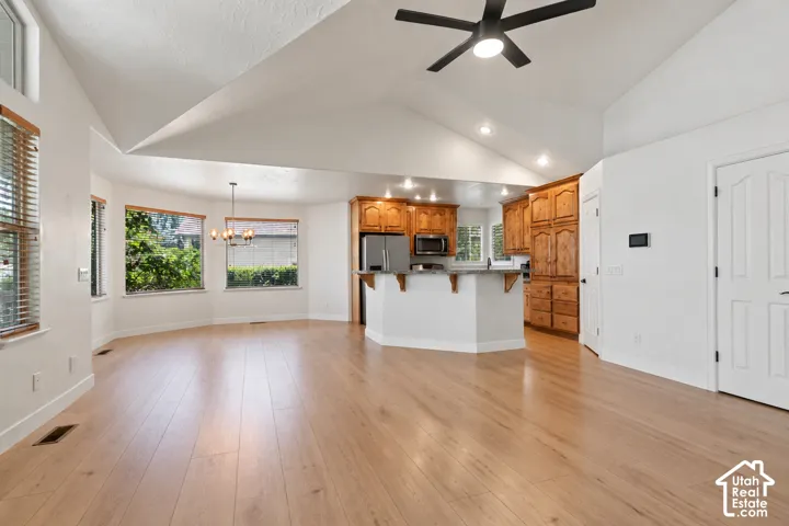 Vaulted ceiling with a black ceiling fan, wood-finish flooring, recessed lighting, and a kitchen featuring wood cabinetry and stainless steel appliances