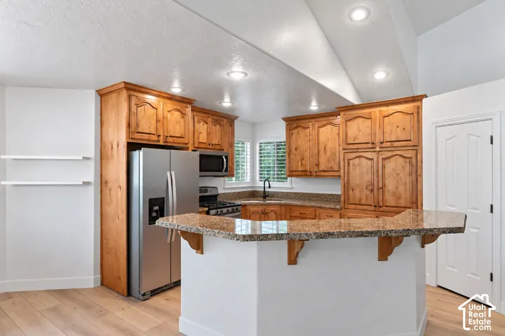 Kitchen featuring wood cabinetry, stainless steel appliances, a corner sink, and a breakfast bar with stone countertops