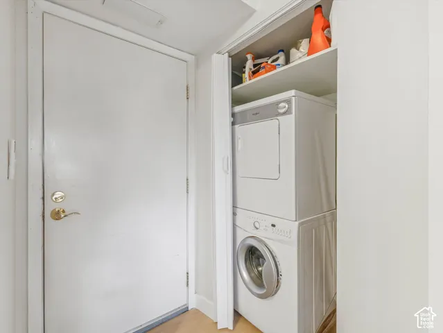 Compact laundry area featuring a stacked washer and dryer unit, built-in shelving, and a solid entry door with brass hardware