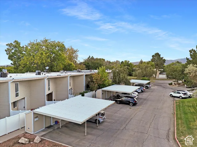 Multi-unit property featuring covered parking structures, paved parking areas, mature landscaping, and mountain backdrop