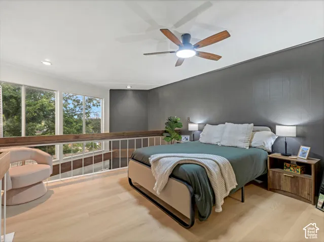 Loft bedroom featuring a wood-finish ceiling fan, recessed lighting, expansive windows, a wood-finish railing, and light wood-finish flooring