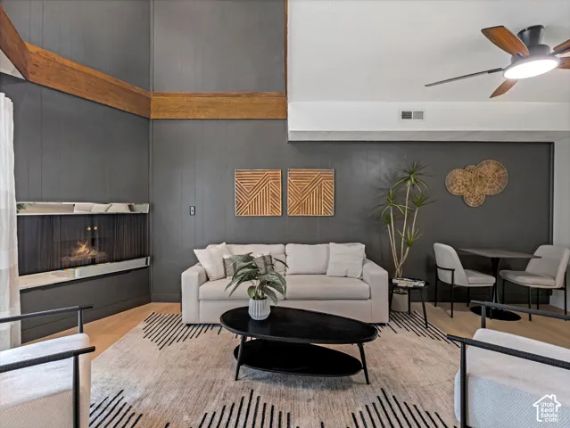 Vaulted ceiling, exposed wood beams, fireplace with a stone surround, wood-finish flooring, and a ceiling fan