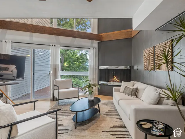 Vaulted ceiling with exposed wood beams, wood-finish flooring, a contemporary fireplace with a marble hearth, and a large sliding glass door