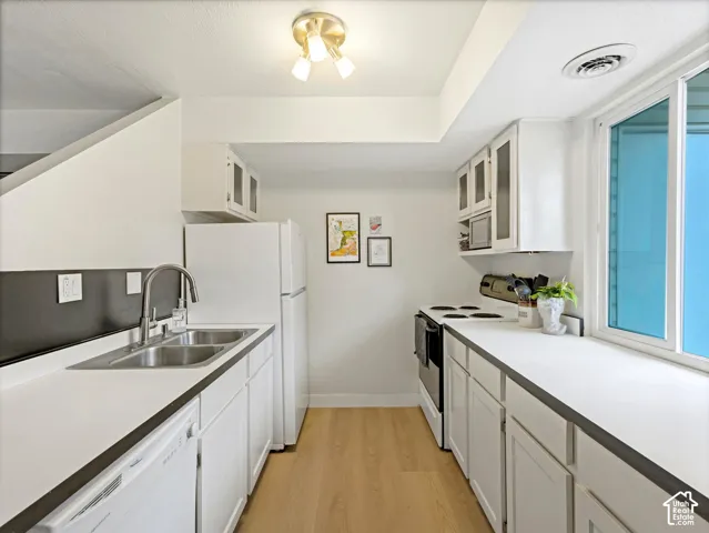 Kitchen featuring wood-finish flooring, white cabinetry, double basin sink, and white appliances