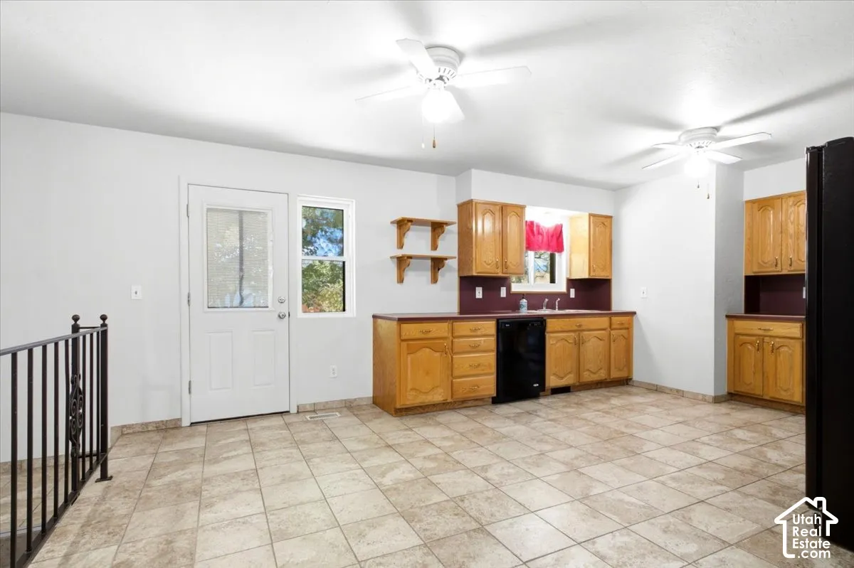 Kitchen area featuring wood cabinetry, tiled flooring, built-in dishwasher, and a sink with a window above