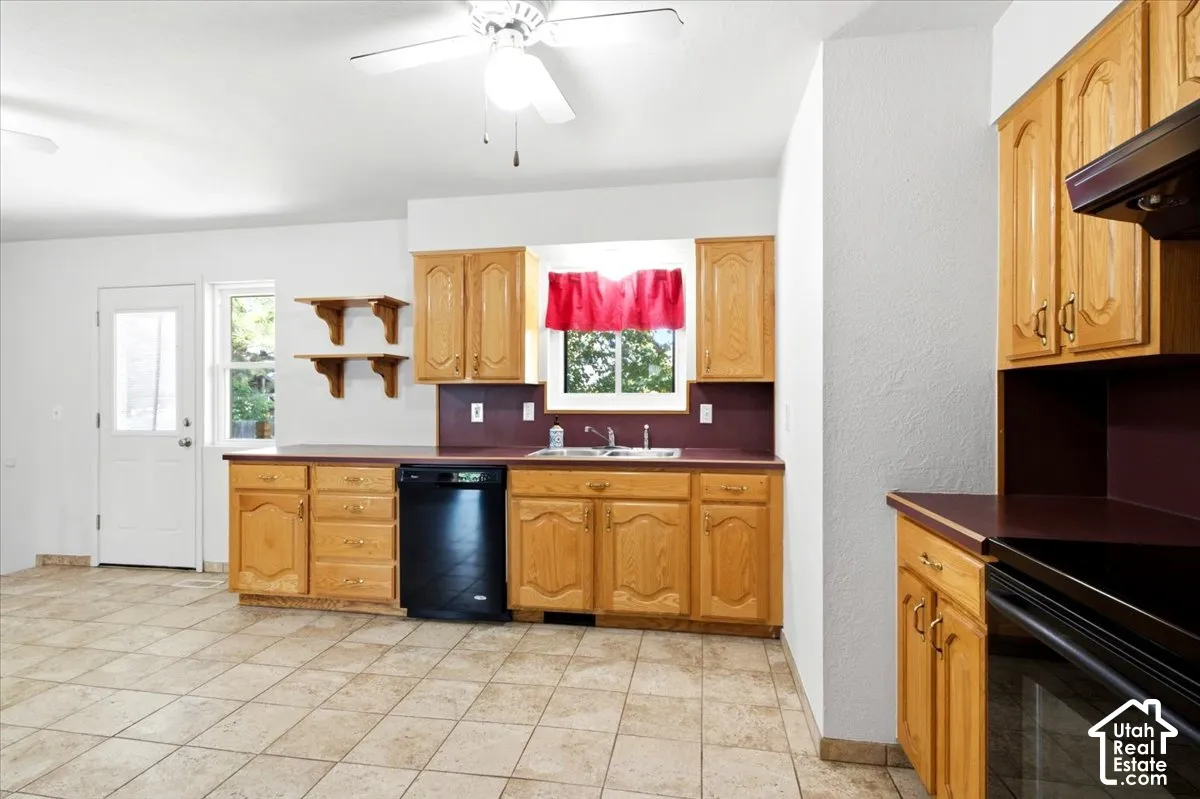 Kitchen featuring wood cabinetry, a double basin sink, black appliances, and neutral tile flooring