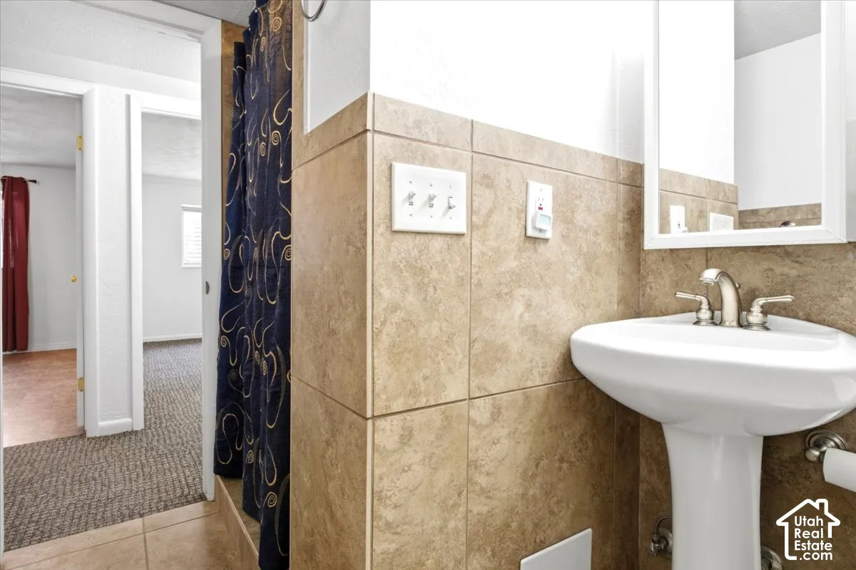Pedestal sink with chrome fixtures, tiled wainscoting, and a wall-mounted mirror