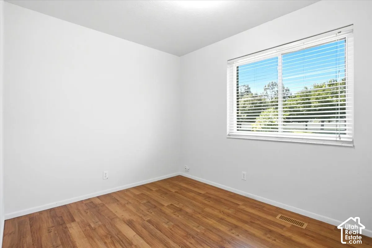 Wood-finish flooring with white walls and a large window featuring horizontal blinds