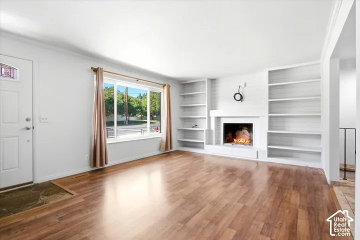 Wood-finish flooring throughout, white built-in shelving, white fireplace with hearth, white paneled accent wall, and a large window