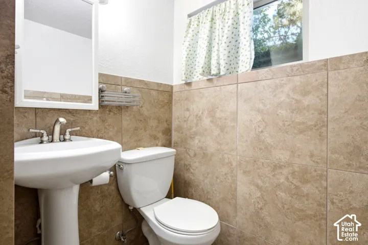 Pedestal sink with chrome faucet, wall-mounted mirror, and ceramic tile wainscoting
