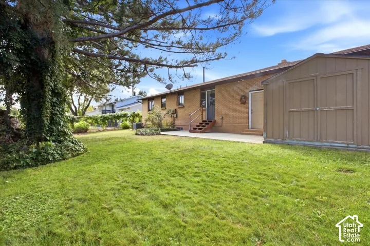Expansive green lawn, mature tree, brick exterior, concrete patio, and exterior storage shed