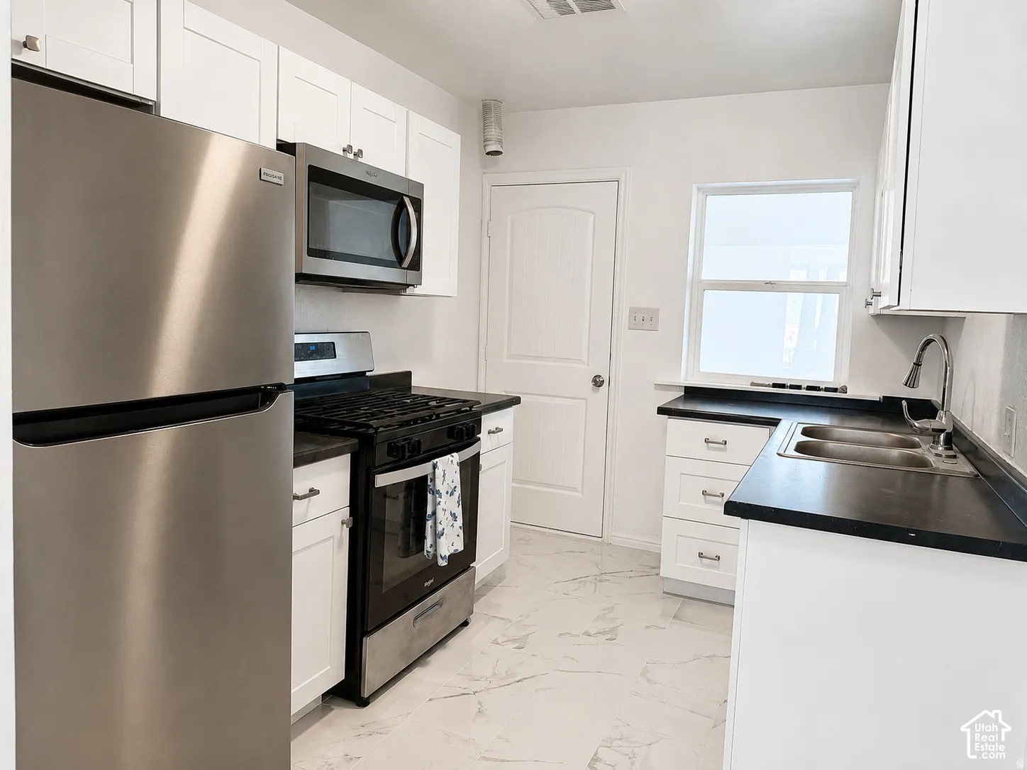 Kitchen featuring stainless steel appliances, white cabinetry, dark countertops, and a dual basin sink with a gooseneck faucet