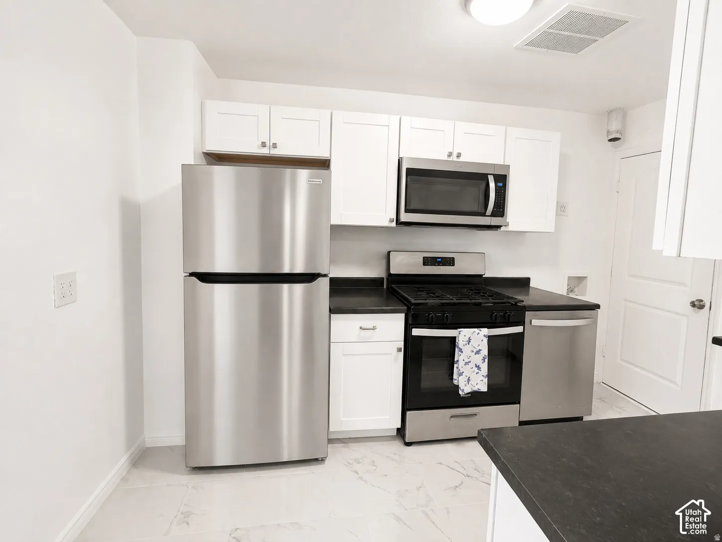 Kitchen featuring white cabinetry, dark countertops, stainless steel appliances, and tile flooring