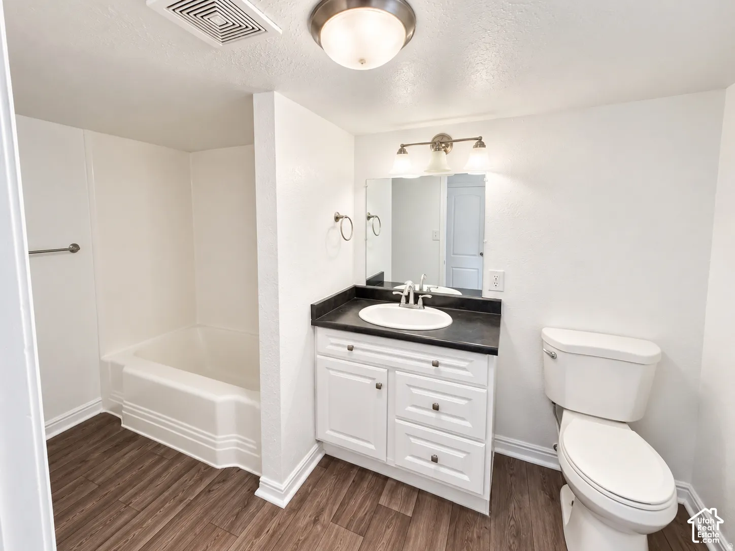 White vanity with ample storage, dark countertop, and a single basin sink