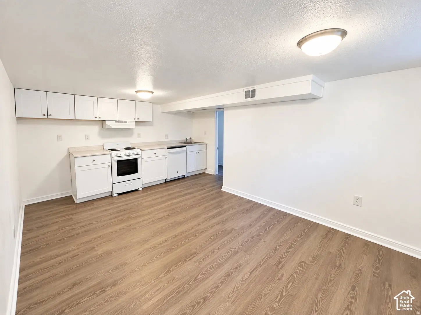 Kitchen area featuring wood-finish flooring, white cabinetry, white electric range, white dishwasher, and light-toned countertops