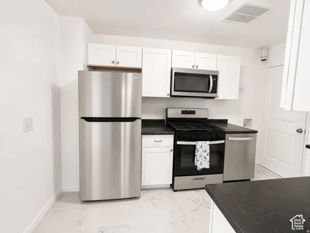 Kitchen featuring white cabinetry, dark countertops, stainless steel appliances, and tile flooring