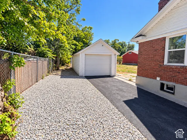 Detached garage with white siding, asphalt driveway, and gravel parking area