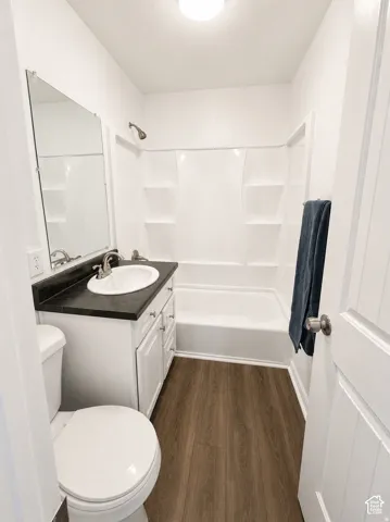 Bathroom featuring a white vanity with a dark countertop, an integrated sink, a full-size mirror, a shower-over-bath unit, and wood-finish flooring