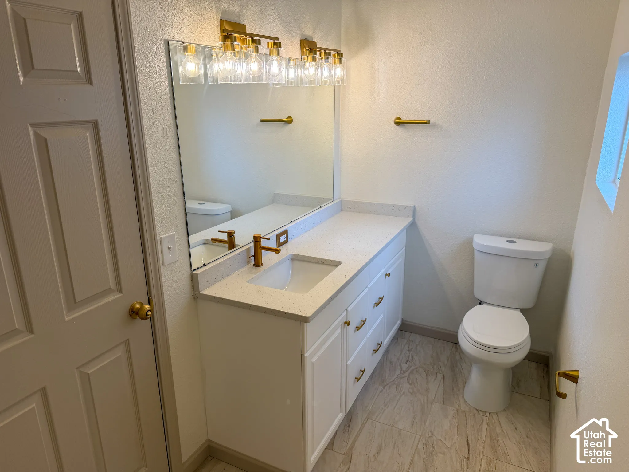 White vanity with gold-tone hardware, a rectangular undermount sink, and a light-toned countertop