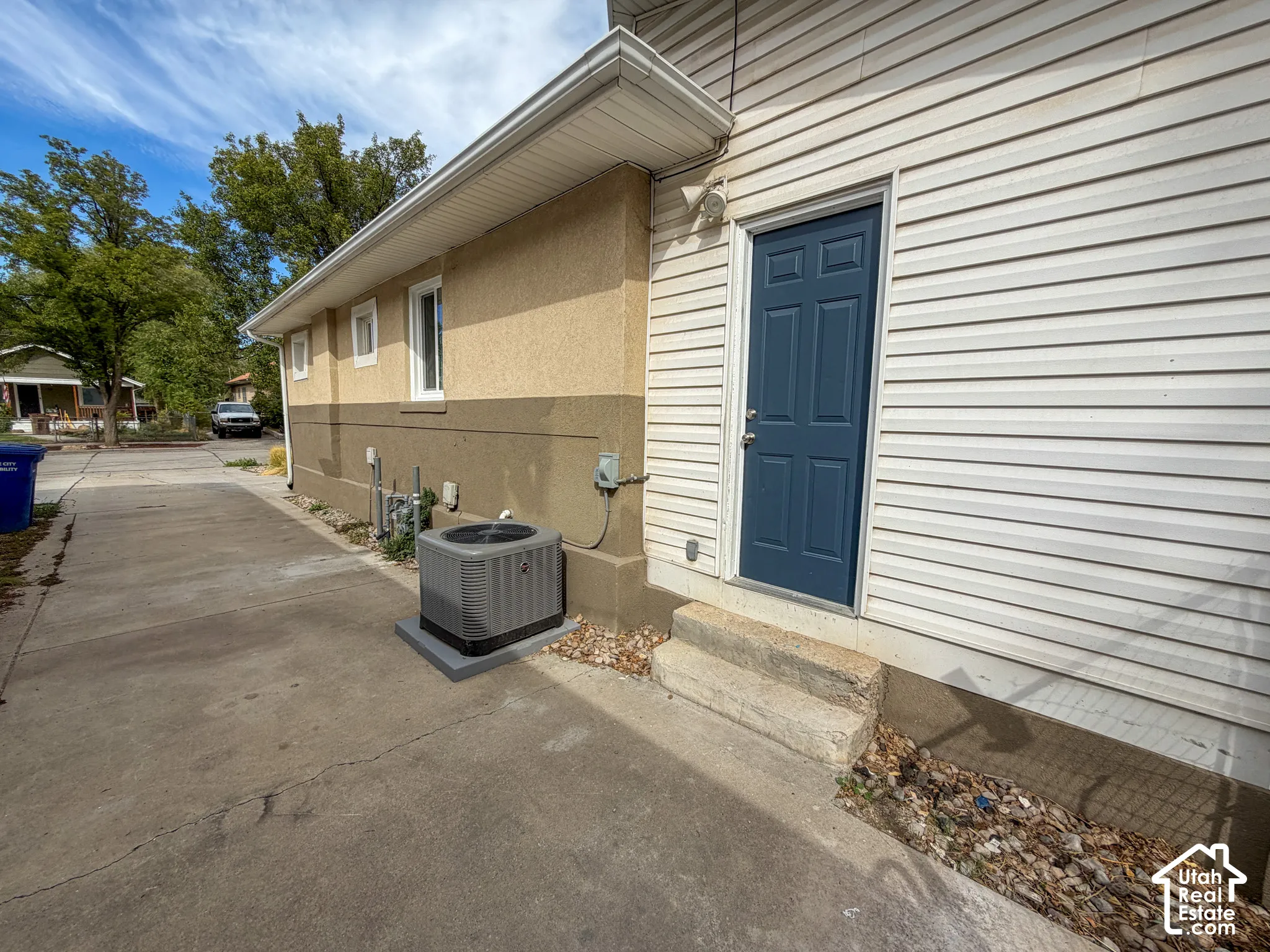 Two-tone exterior with stucco and siding finishes, featuring a dark blue entry door, concrete steps, and a concrete driveway