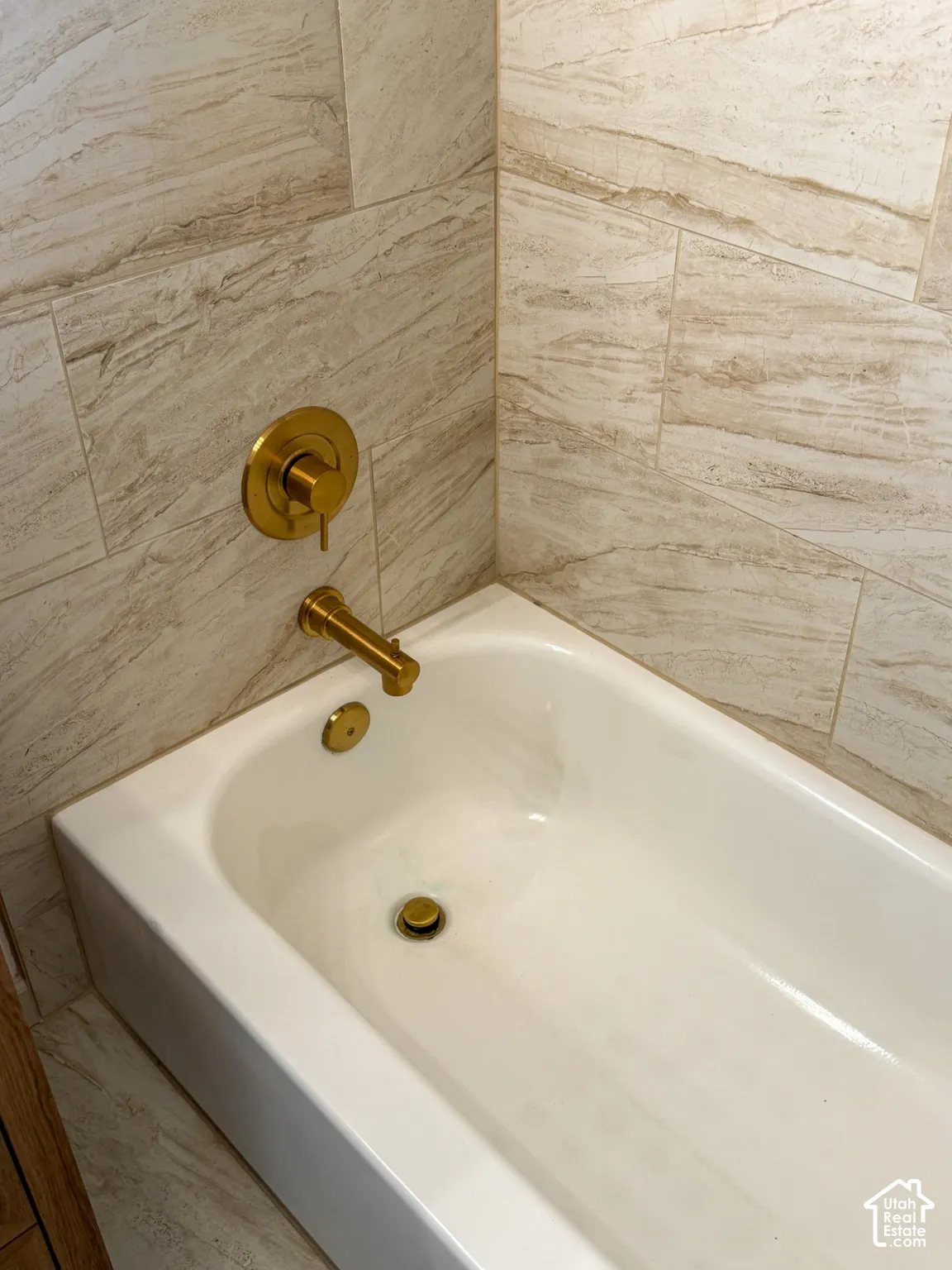 Soaking tub with brass-finish fixtures and stone-look tiled surround