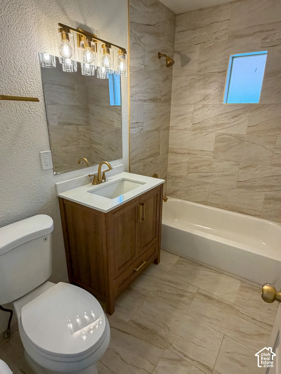 Bathroom featuring a wood-finish vanity with an integrated basin, gold-tone fixtures, a built-in bathtub, and ceramic wall and floor tiling