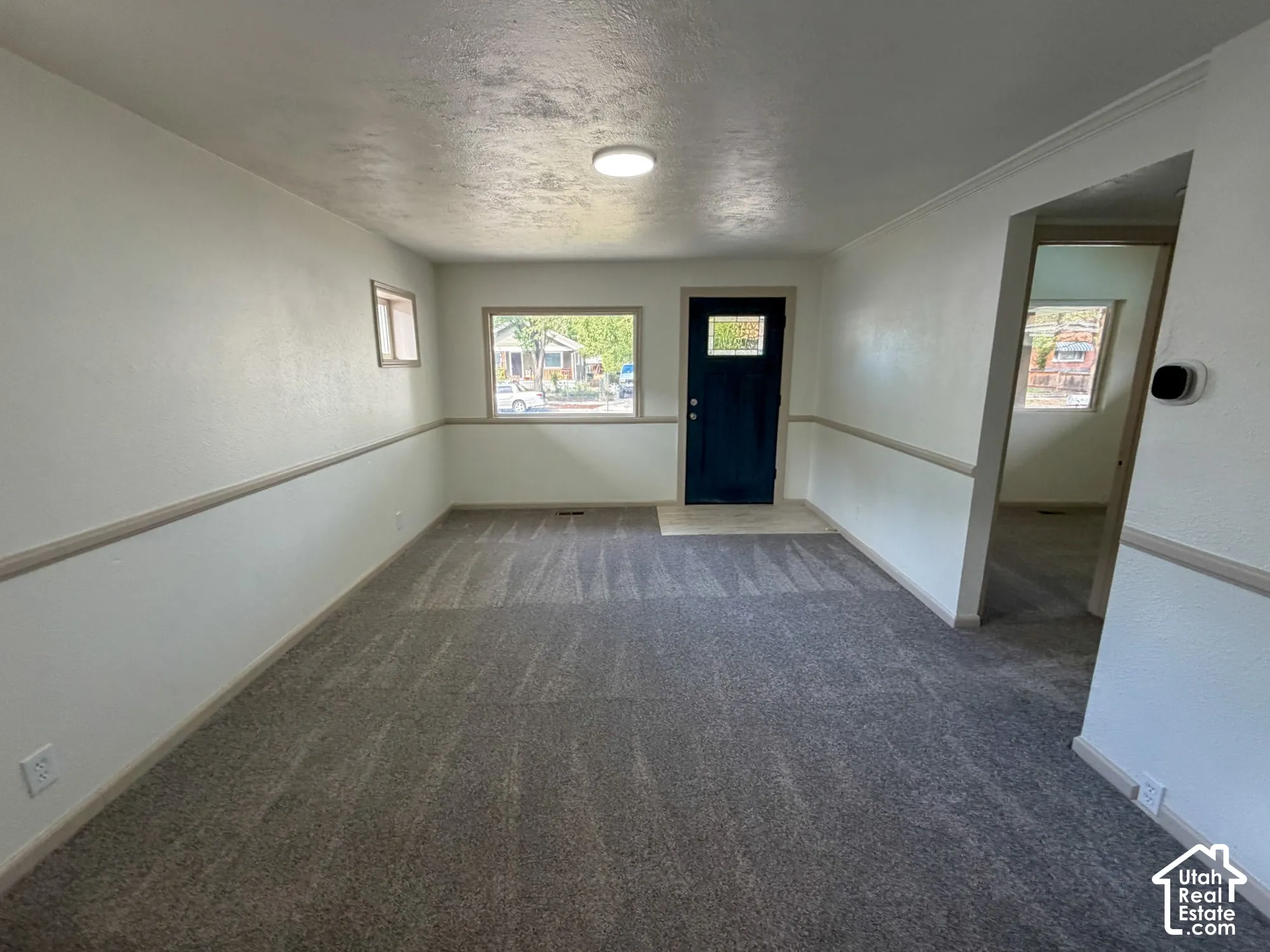 Spacious room with gray patterned carpeting, white walls, and a prominent front entry door