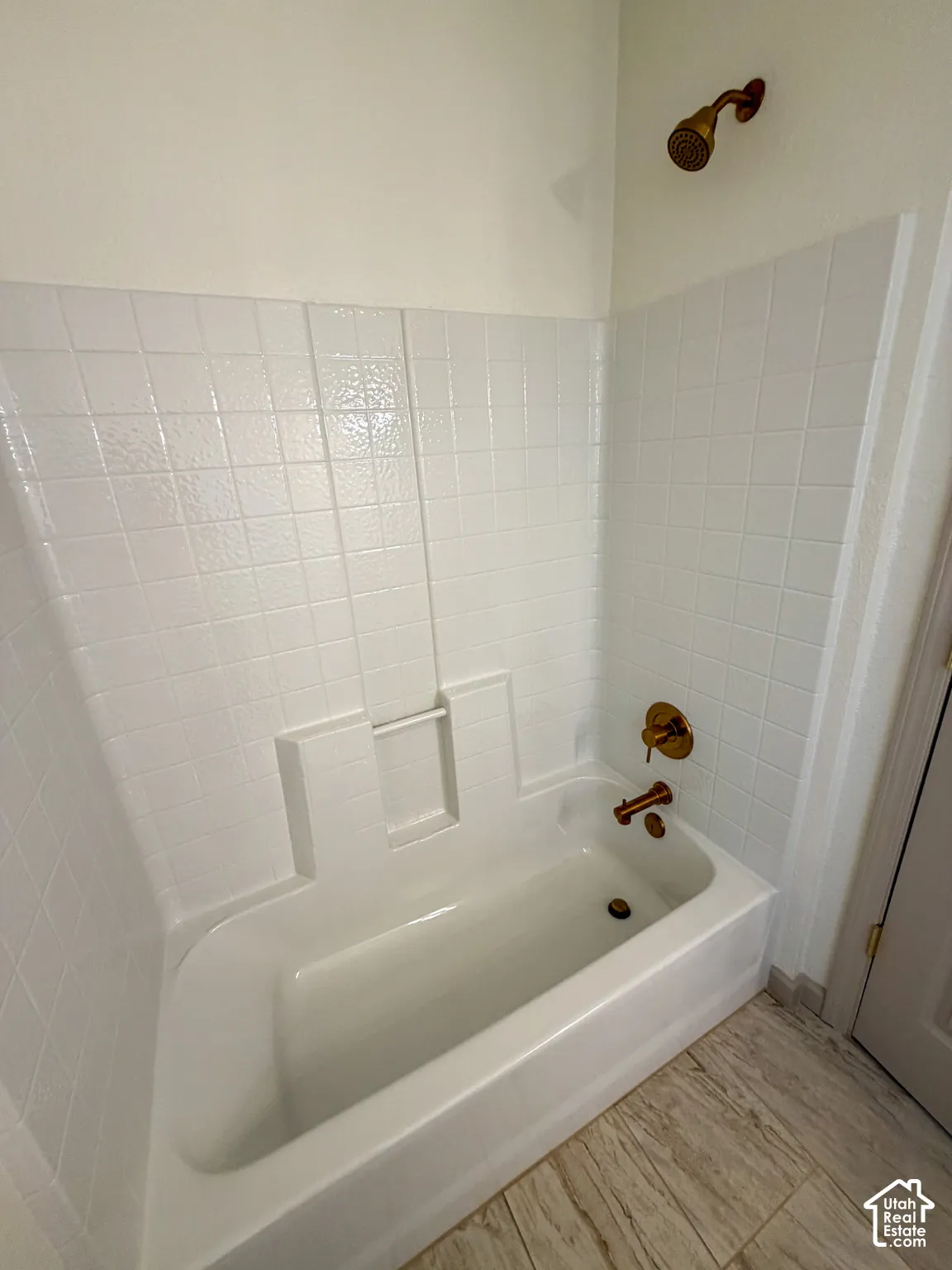 White bathtub with integrated shower, white tiled surround, and brass-finish fixtures