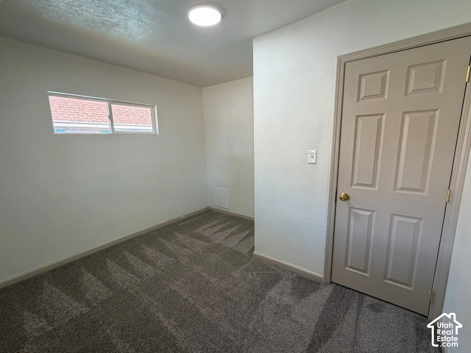 Recessed window, textured walls, overhead flush-mount lighting, and neutral tone carpeting