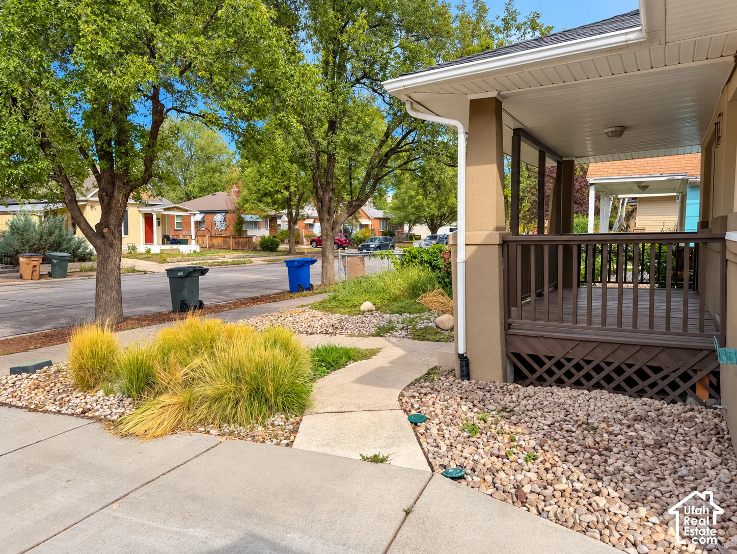 Covered porch with wood railing, concrete pathway, and decorative rock landscaping with planted grasses