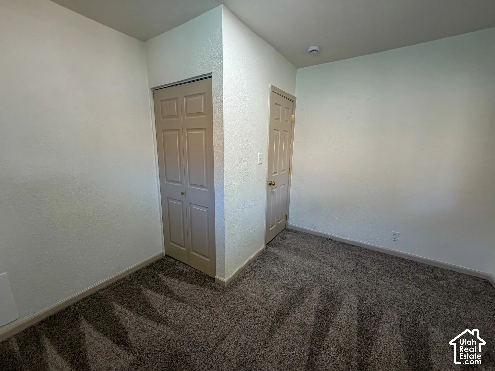 Interior space featuring textured walls, carpet flooring, a bifold closet door, and an additional standard door