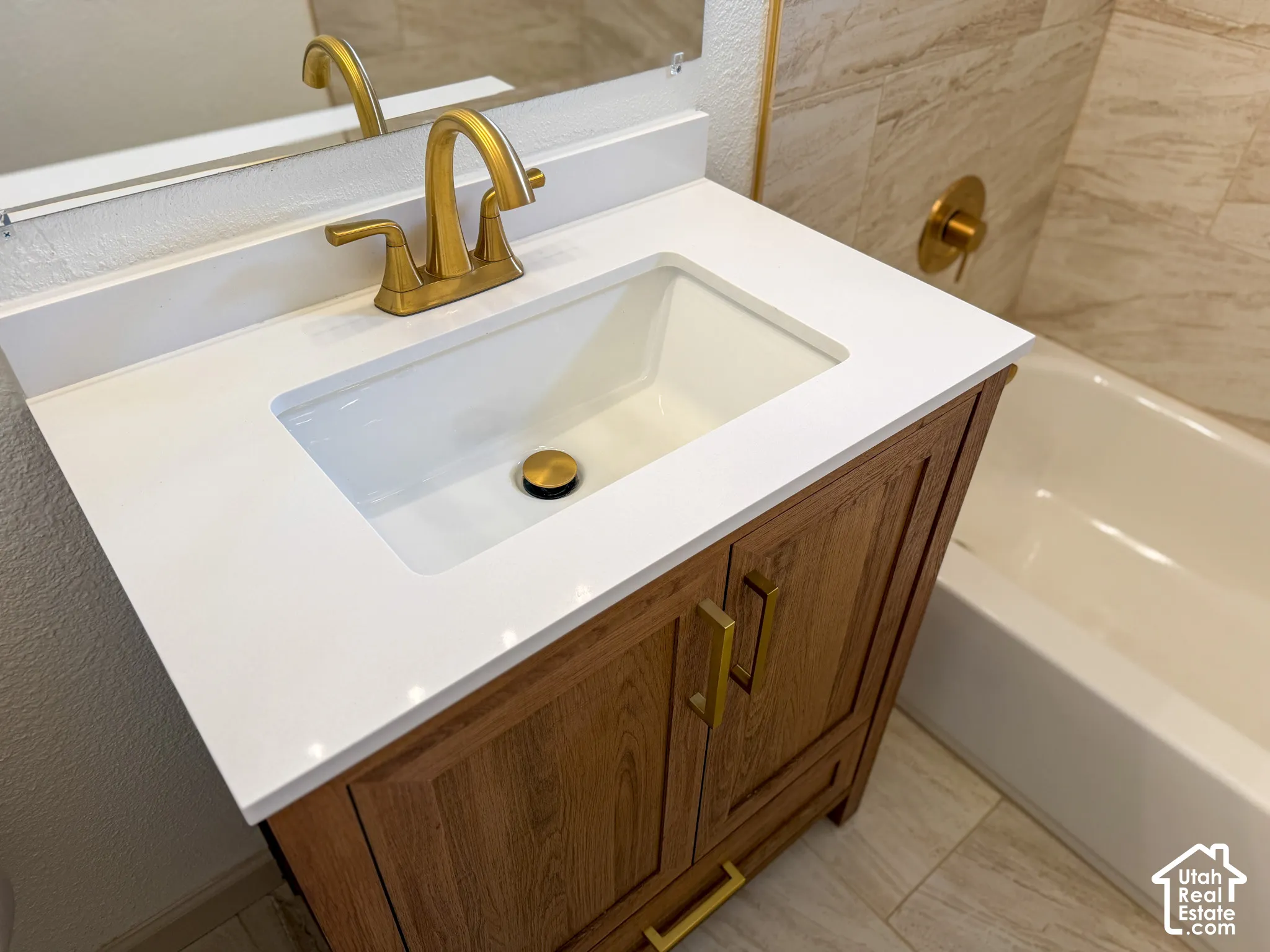 Wood-finish vanity with gold hardware, white countertop with integrated sink, and gold-finish faucet