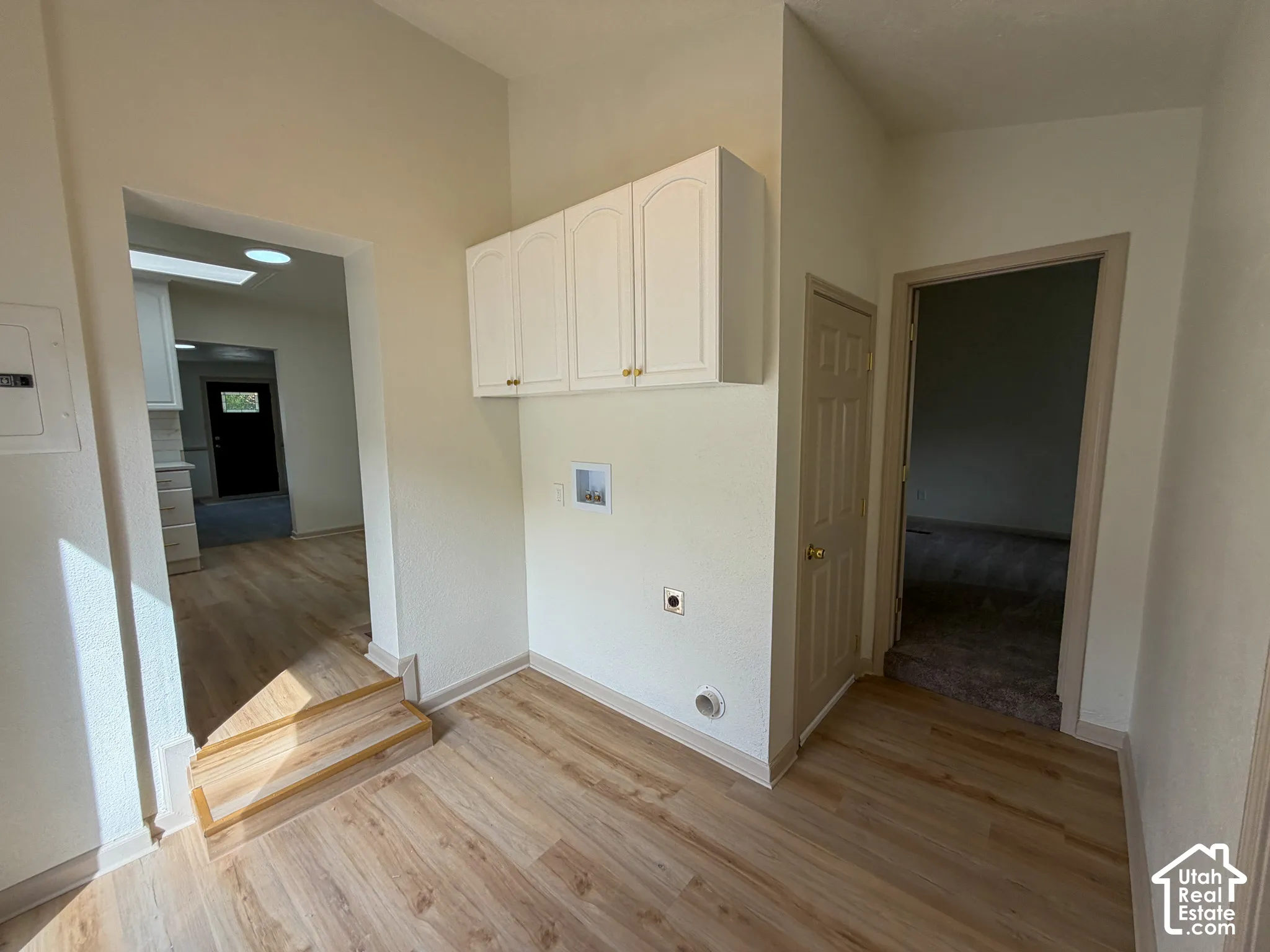 Wood-finish flooring with white baseboards, built-in white cabinetry, and a white interior door with a brass-finish knob