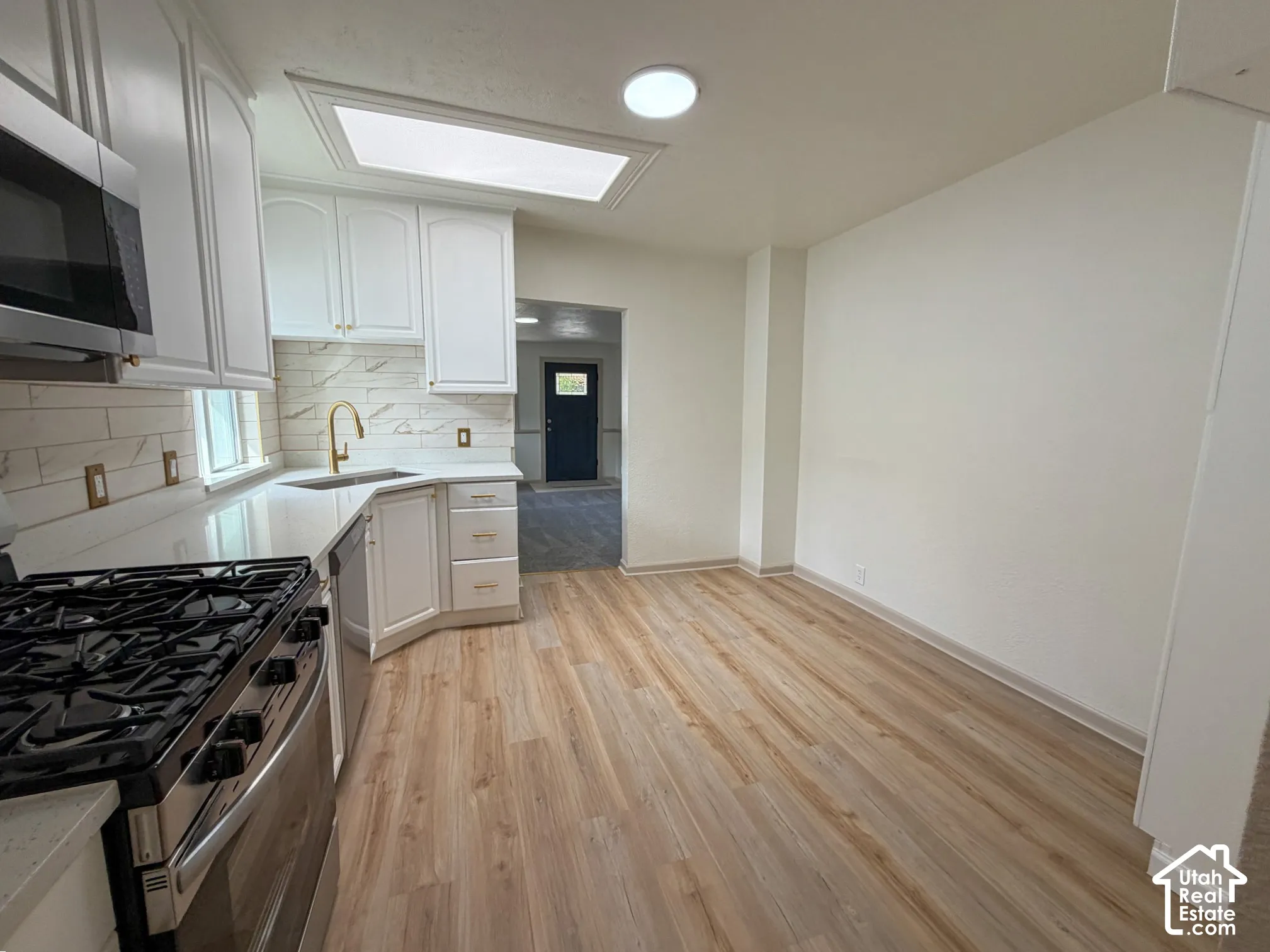 Kitchen featuring white cabinetry, wood-finish flooring, stainless steel appliances, a skylight, and a gold-tone faucet