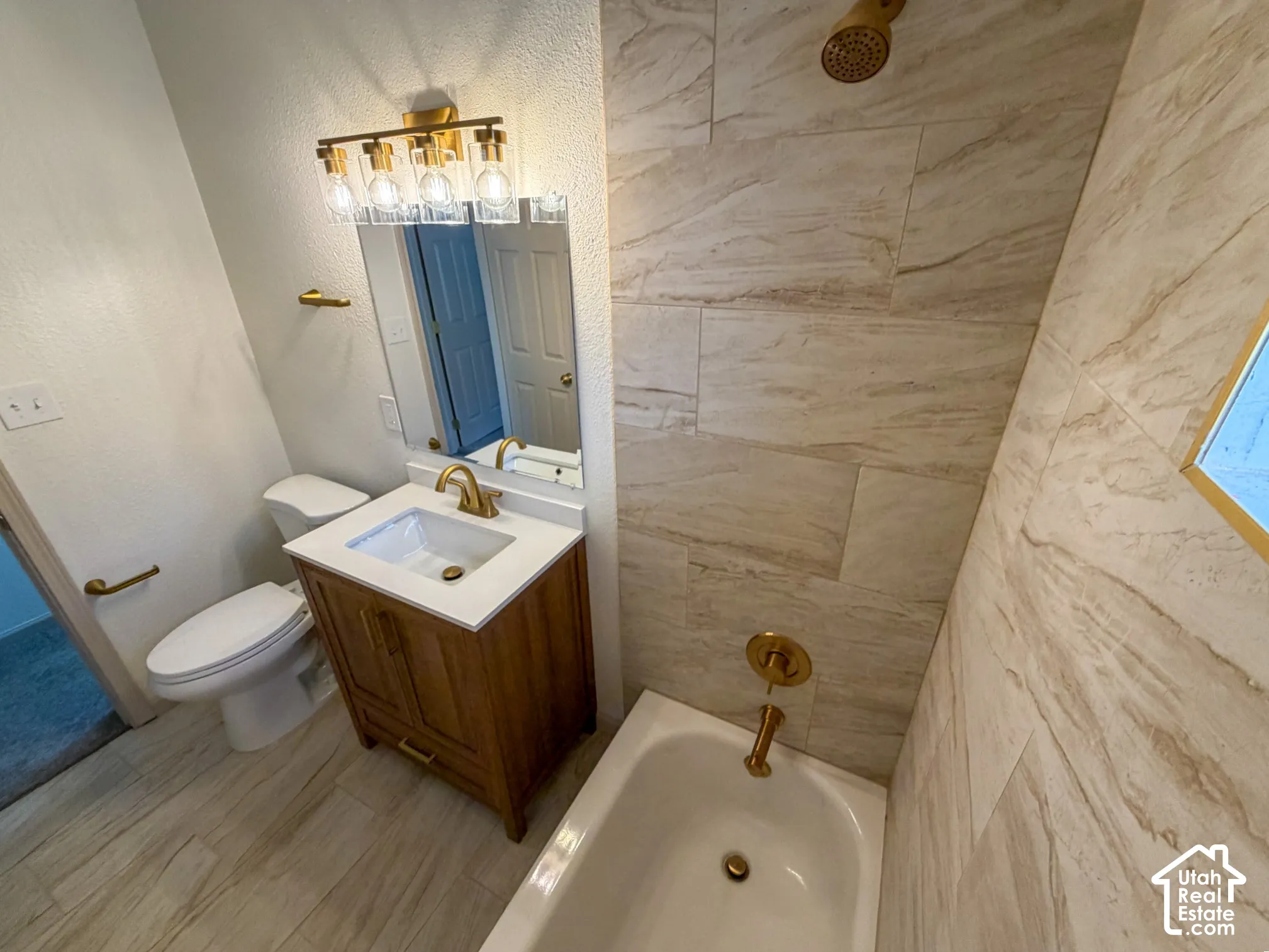 Bathroom featuring a wood-finish vanity with an integrated sink, a built-in bathtub, and floor-to-ceiling tiled walls