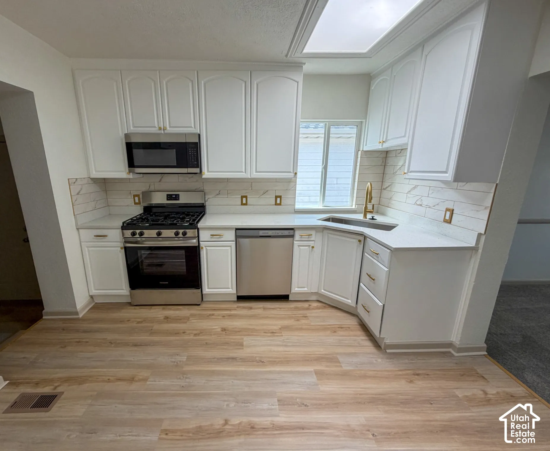 Kitchen featuring white cabinetry, stainless steel appliances, light-toned countertops, a skylight, and wood-finish flooring