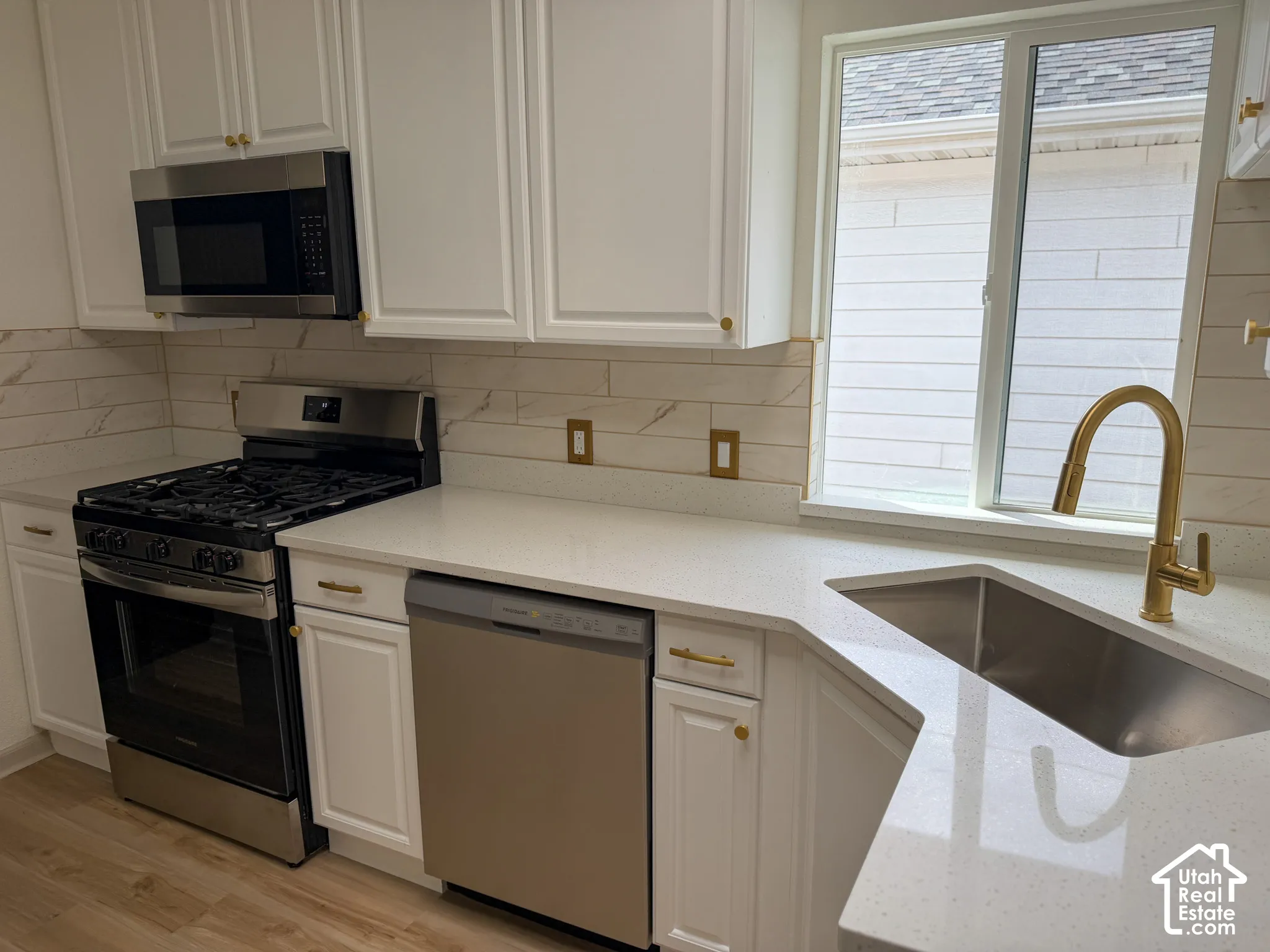 White cabinetry, stainless steel appliances, light-toned countertops, and a gold-finish faucet