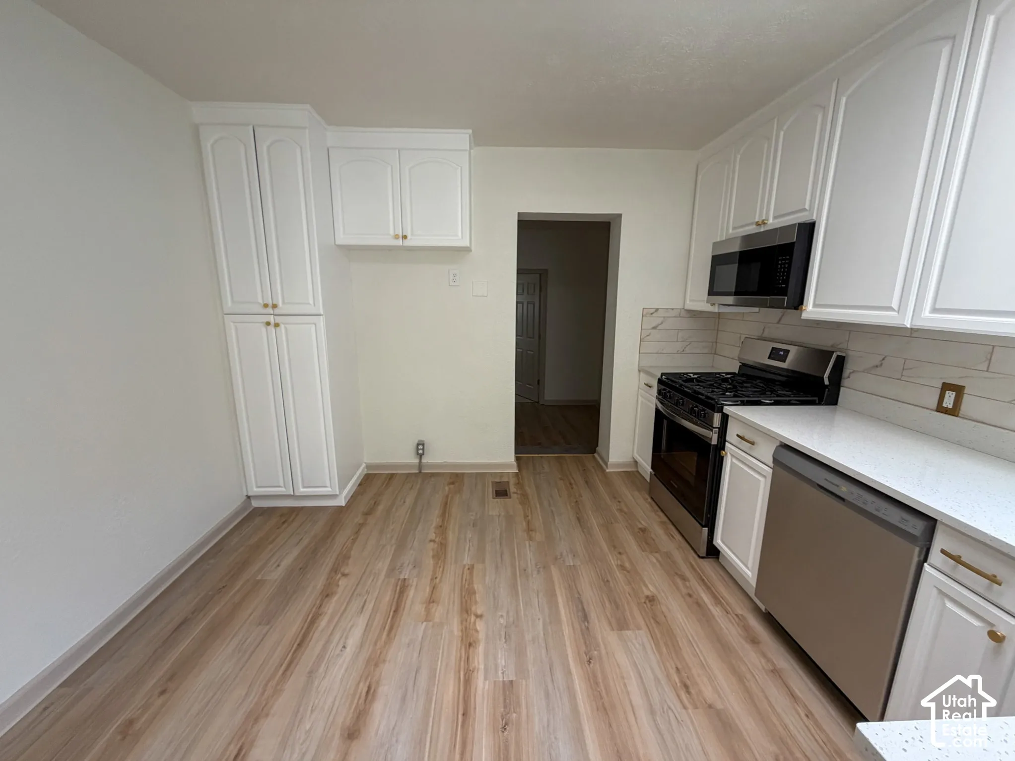 White cabinetry, wood-finish flooring, stainless steel appliances, white countertops, and a white tile backsplash