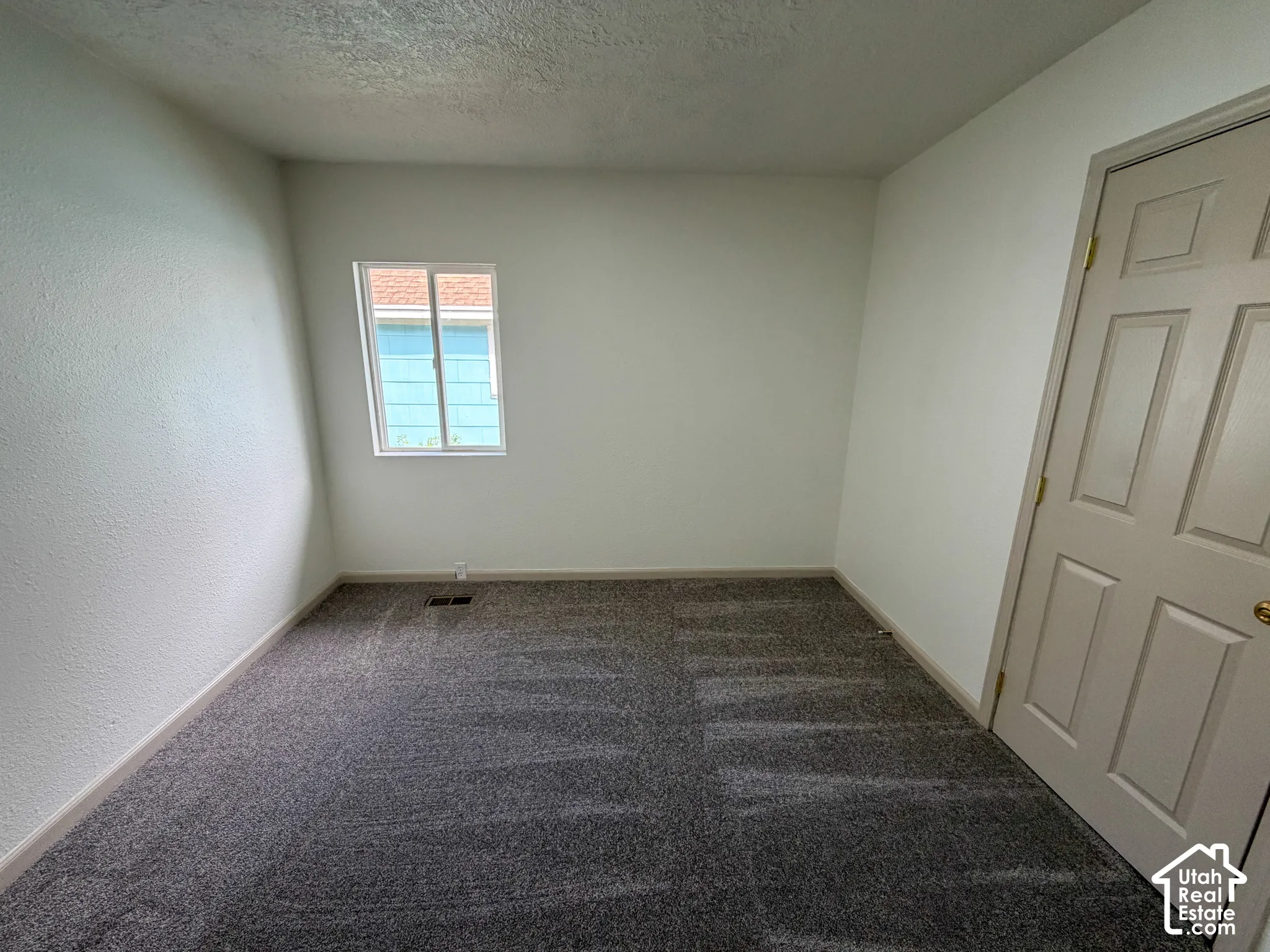 Neutral wall paint, textured walls, carpet flooring, single window, paneled door