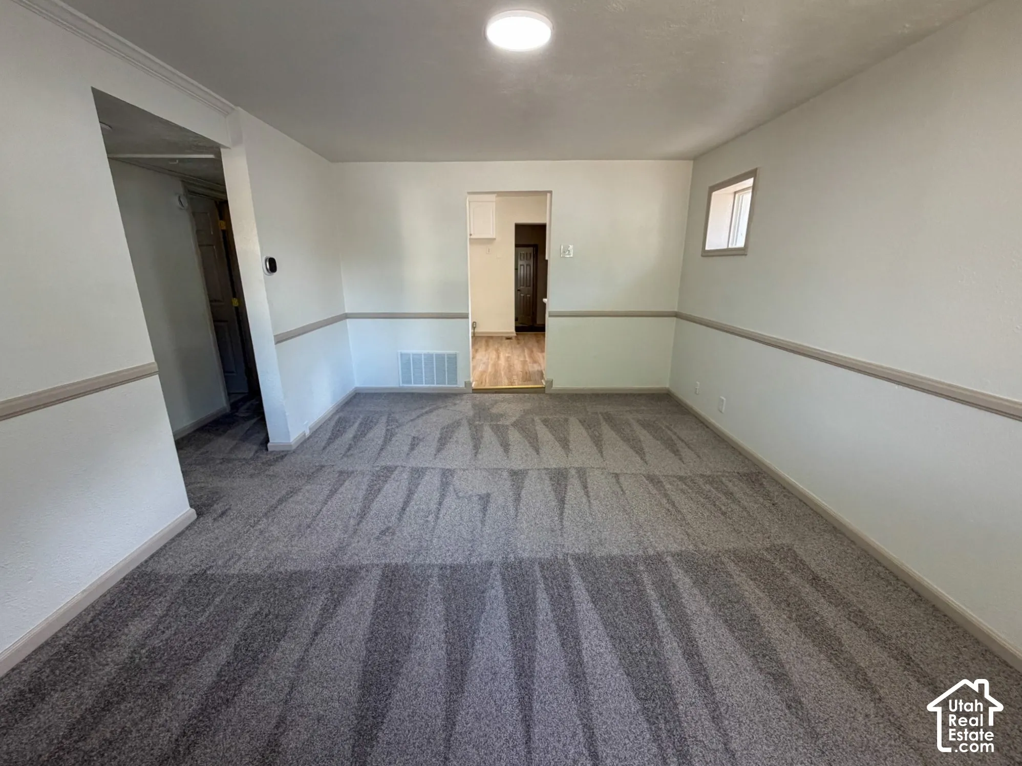 Recessed ceiling light, neutral wall colors, chair rail molding, patterned carpet flooring, and a window for natural light