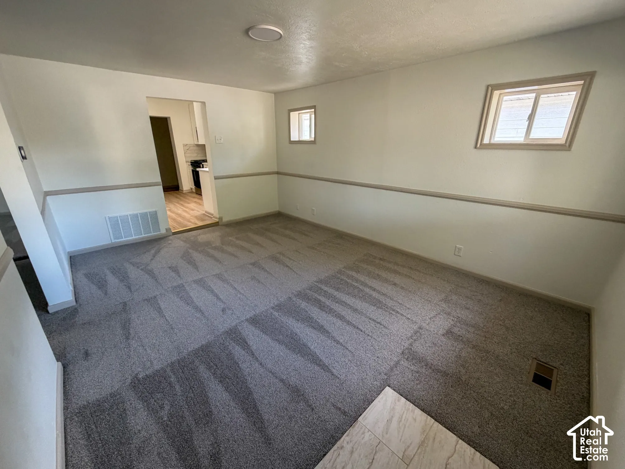 Carpeted flooring, recessed ceiling lighting, two windows, and a doorway to an adjacent room with wood-finish flooring