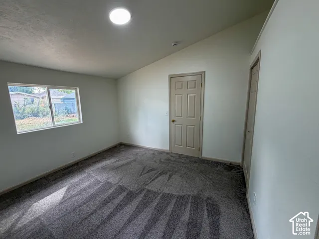 Vaulted ceiling with an overhead light fixture, light-colored walls, window with outdoor scenery, and patterned carpet flooring