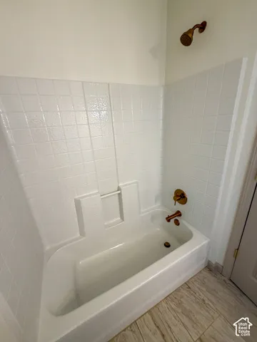 White bathtub with integrated shower, white tiled surround, and brass-finish fixtures